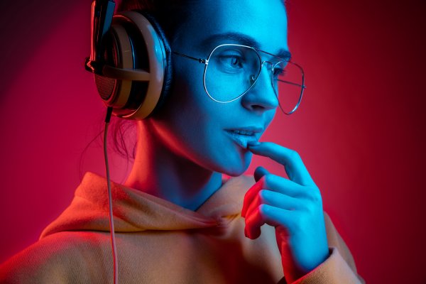 open-back headphones woman with glasses and hoodie wearing headphones red background